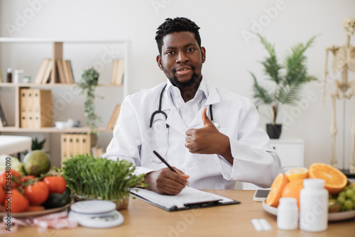 Portrait of dieting expert wearing lab coat and stethoscope looking at camera with serious face expression. Male doctor writing prescription on clipboard paper for patient suffering from gastritis.