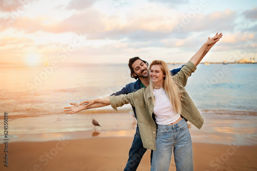 Young couple on beach pretending flying, spreading hands like wings