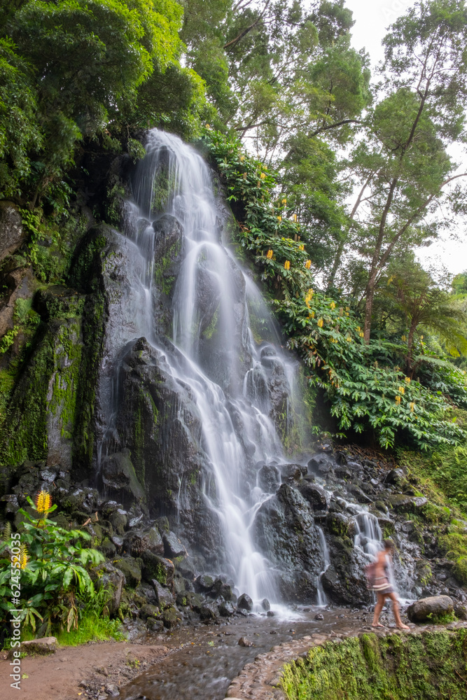 Waterfall in the Botanical Garden of Ribeira do Guilherme in Nordeste with tourists, Sao Miguel island in the Azores.