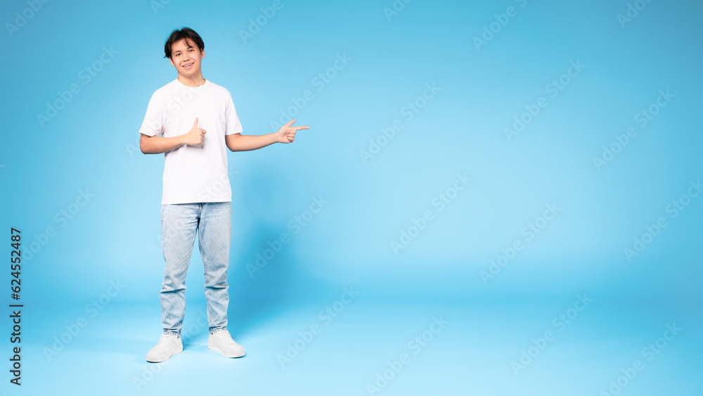Chinese guy pointing aside gesturing thumbs up on blue background Chinese guy pointing aside gesturing thumbs up on blue background