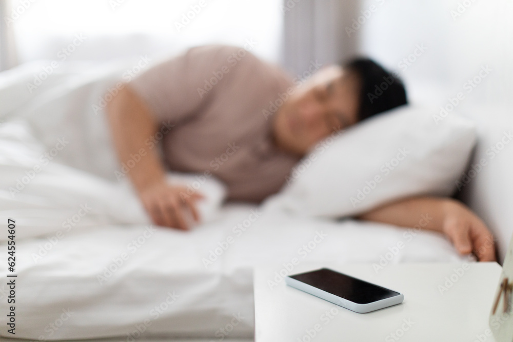 Selective focus on smartphone on bedside near asian man sleeping Selective focus on smartphone on bedside near asian man sleeping
