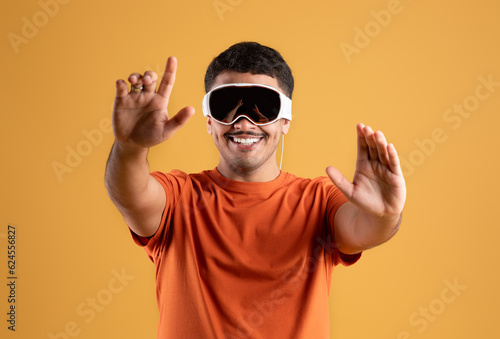 Modern imaging. Happy handsome brazilian man using modern vision pro glasses of virtual reality on yellow background