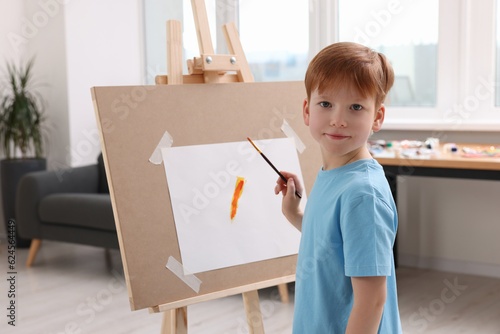 Little boy painting in studio. Using easel to hold canvas