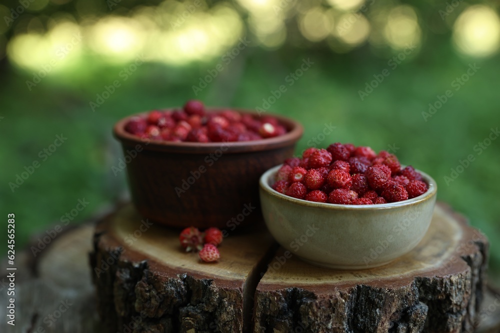 Bowls of tasty wild strawberries on stump against blurred background, closeup Bowls of tasty wild strawberries on stump against blurred background, closeup