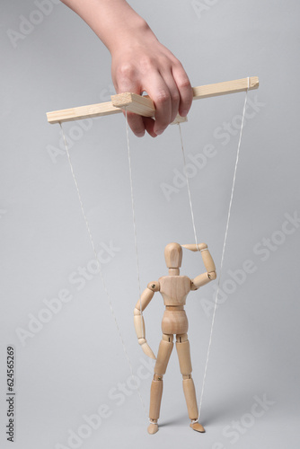 Woman pulling strings of puppet on light grey background, closeup photo