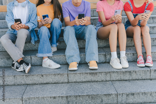 Fototapete Cropped picture of group teenagers holding mobile phones watching video, communication online, chatting sitting on the street