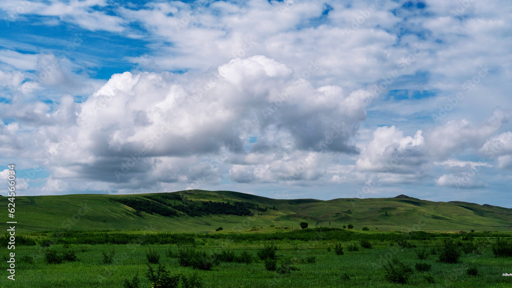 Photo of the steppe in summer, with beautiful clouds in the blue sky, the endless steppe at the foot of high hills under a warm summer sky. Khakassia, Siberia, Russia.
