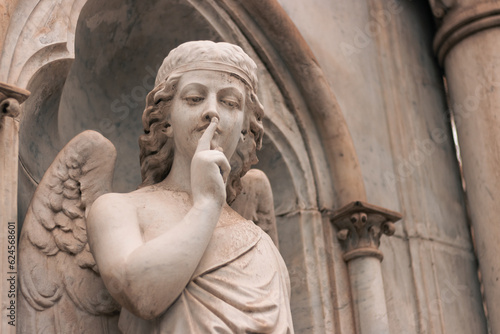 religious statue figure of an angel making silence on a grave in an outdoor cemetery
