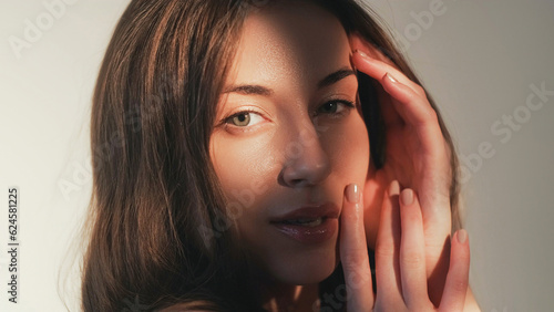 Female skincare. Model posing. Woman elegance. Sensual gentle beautiful lady enjoying sunlight shadow hands touching perfect fresh flawless face skin isolated on beige.