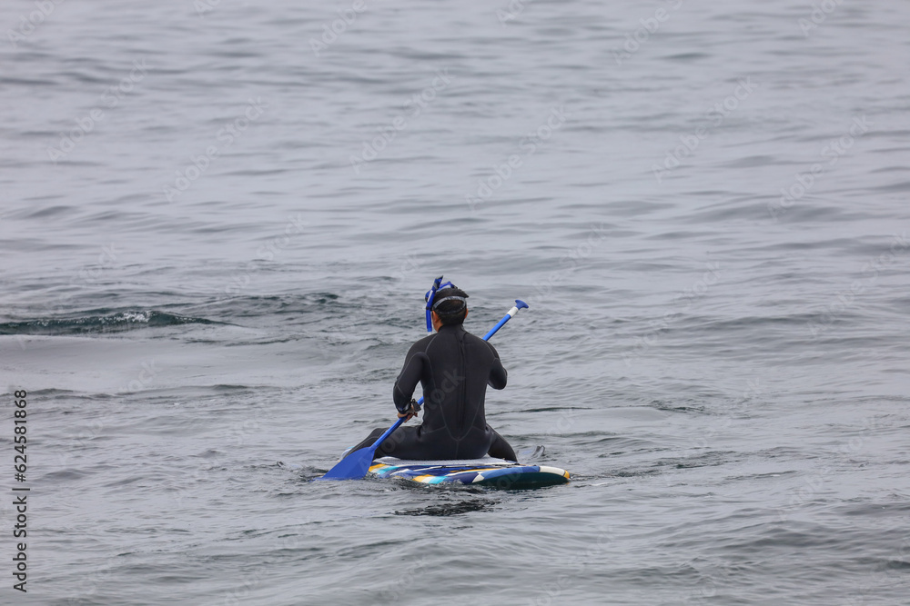 A person wearing a wet suit and snorkeling gear floating on a paddle board in the ocean.