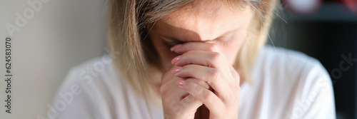Stressed sad woman with closed eyes keeps her hands connected near her face close-up.