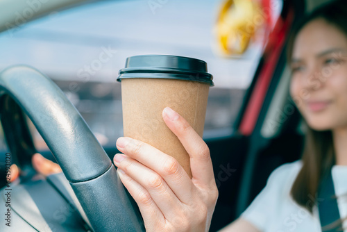 Young woman driving and holding a paper coffee cup to relieve sleepiness. photo