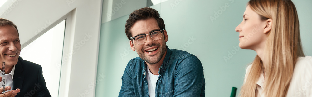 We have great results Young handsome man in eyeglasses discussing something with colleagues and smiling while sitting in the modern office We have great results Young handsome man in eyeglasses discussing something with colleagues and smiling while sitting in the modern office