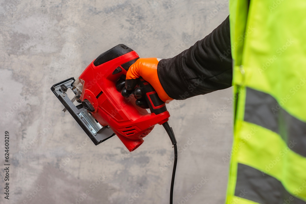 Male worker holds a close-up jigsaw electric in his hands against the background of a concrete wall.