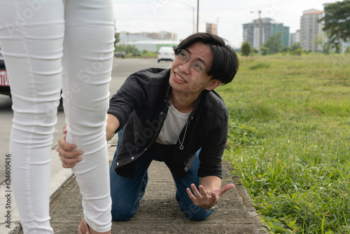 A pitiful young man kneels down and grabs his girlfriend's leg in a desperate attempt to prevent her from leaving him. Breaking up with a weak or insufferable guy
