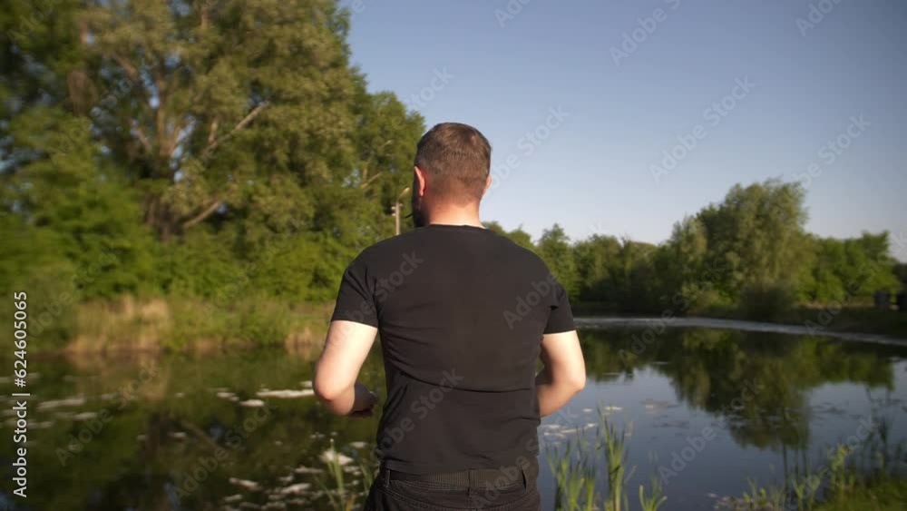 Close-up unrecognizable male outdoors on cloudy summer morning on background of landscape. a young bearded man in a black T-shirt watching at the river Close-up unrecognizable male outdoors on cloudy summer morning on background of landscape. a young bearded man in a black T-shirt watching at the river