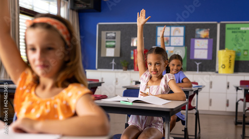 Diverse elementary schoolchildren raising hands at desks in class