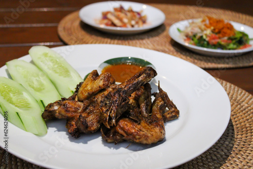 Ayam taliwang or taliwang chicken, a traditional roasted chicken dish from Lombok usually served with beberuk and water spinach plecing. Served with white plate on a wood background