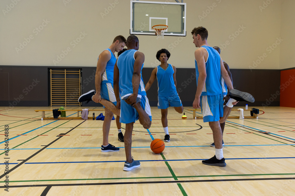 Diverse male basketball players stretching and warming up at gym