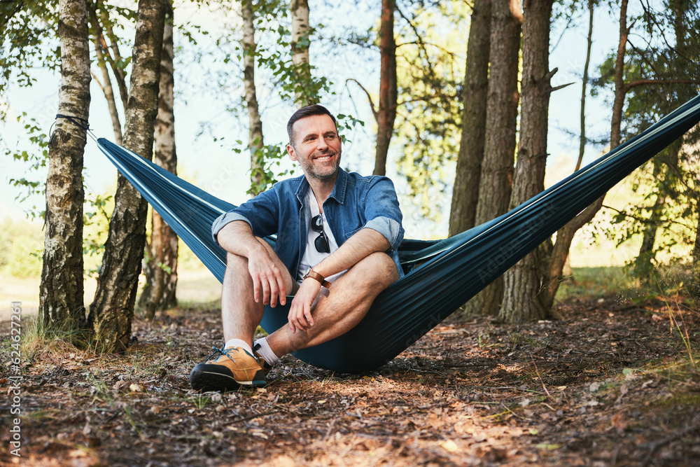 © baranq - Mid adult man enjoying summer trip sitting in hammock in forest