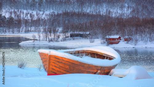 Beautiful winter landscape with old fishing red cabin (boathouse) boat at sunset - Red wooden boathouse and boat covered with layers of snow - Tromso, Norway