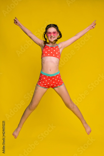 tweens happy girl in swimsuit jumping on yellow background. love summertime content photo