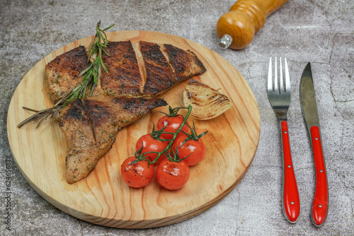 roasted iberian secreto iberico with cherry tomato, roasted onion, pepper and cutlery on a wooden plate. photo