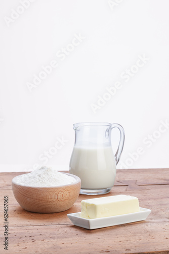 glass jug with milk and wooden bowl with white flour and butter