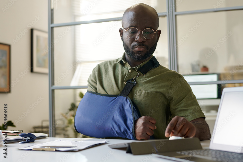Fototapeta premium African American man with injury using tablet pc while sitting in office of social service