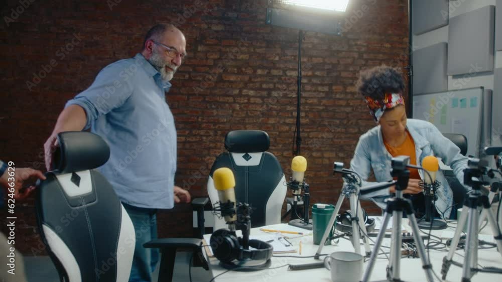 Group of diverse podcast co-hosts entering recording studio, greeting each other with handshakes, sitting at table with audio equipment and putting headphones on Group of diverse podcast co-hosts entering recording studio, greeting each other with handshakes, sitting at table with audio equipment and putting headphones on