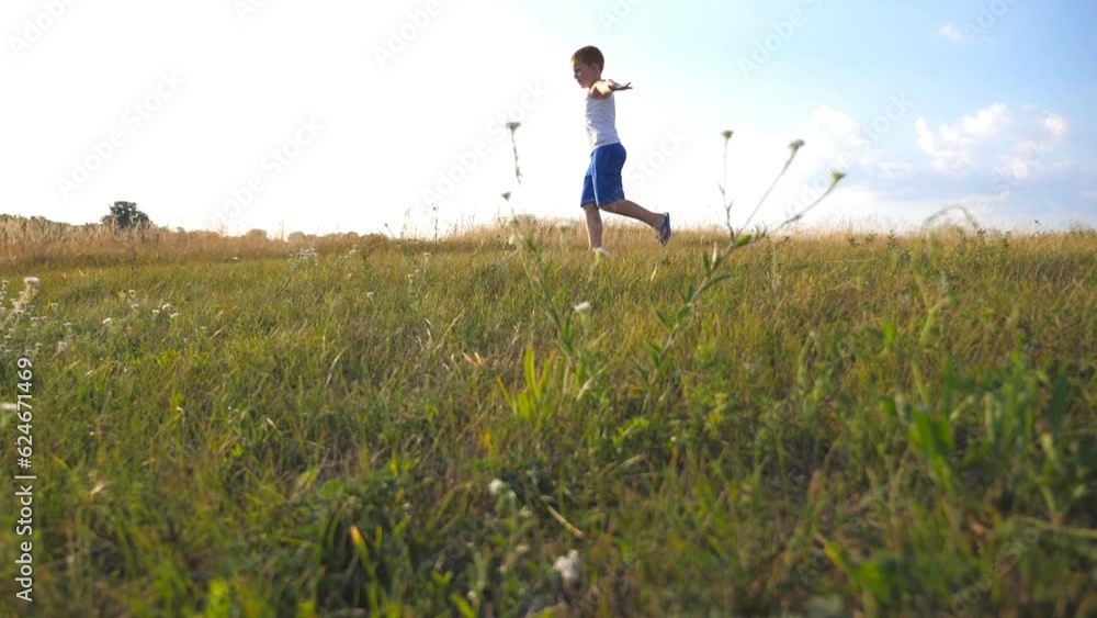 Young boy with raised hands running on green grass at the field on sunny day. Child jogging at the lawn outdoor. Happy smiling male kid having fun in nature on a summer meadow. Slow motion Close up Young boy with raised hands running on green grass at the field on sunny day. Child jogging at the lawn outdoor. Happy smiling male kid having fun in nature on a summer meadow. Slow motion Close up