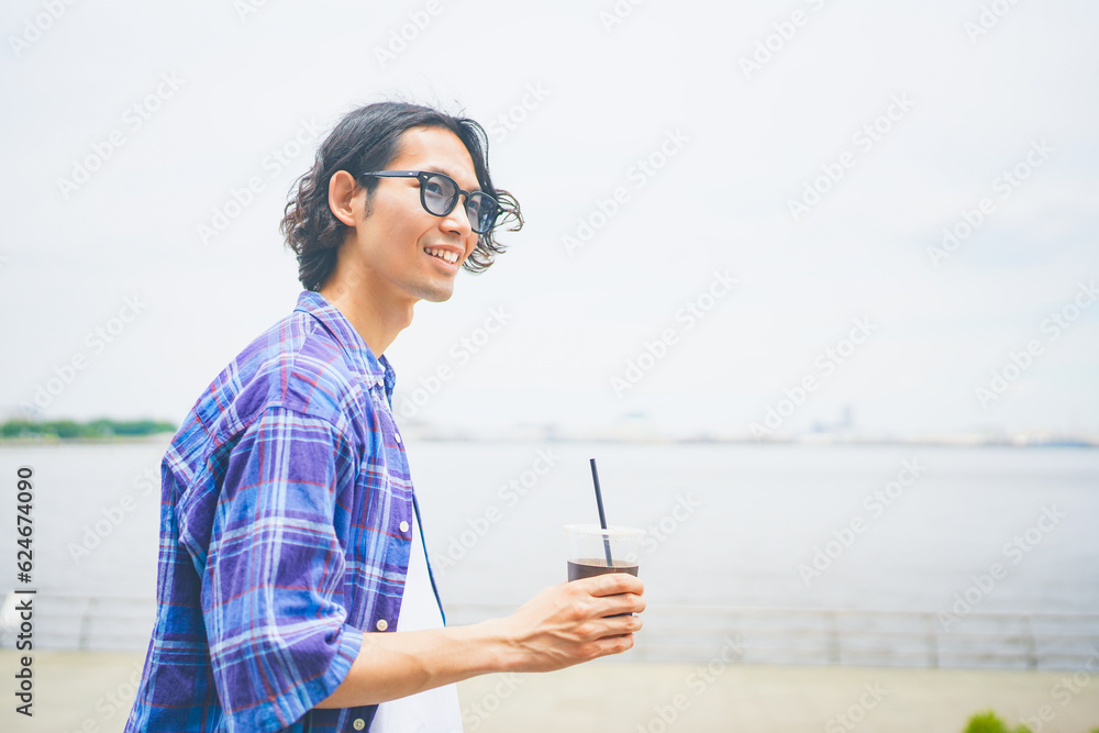 テイクアウトしたコーヒーを片手に海辺を歩く男性