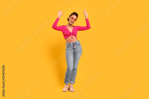 Happy young woman in stylish sunglasses dancing on orange background © New Africa