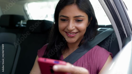 Happy young indian woman using cell phone sitting in the back seat of a car. Technology and transport concept.
