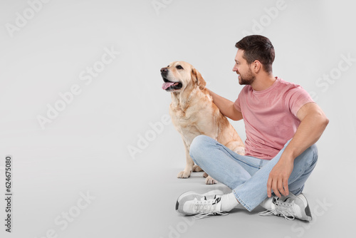 Man with adorable Labrador Retriever dog on light gray background, space for text. Lovely pet