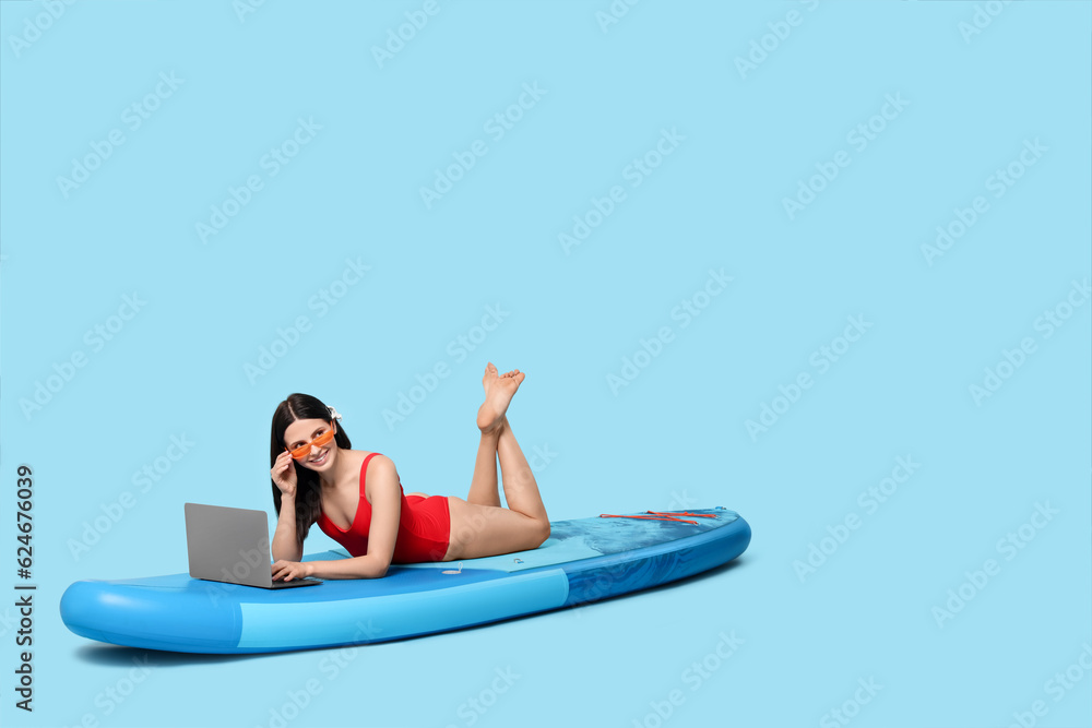 Happy woman with laptop on SUP board against light blue background