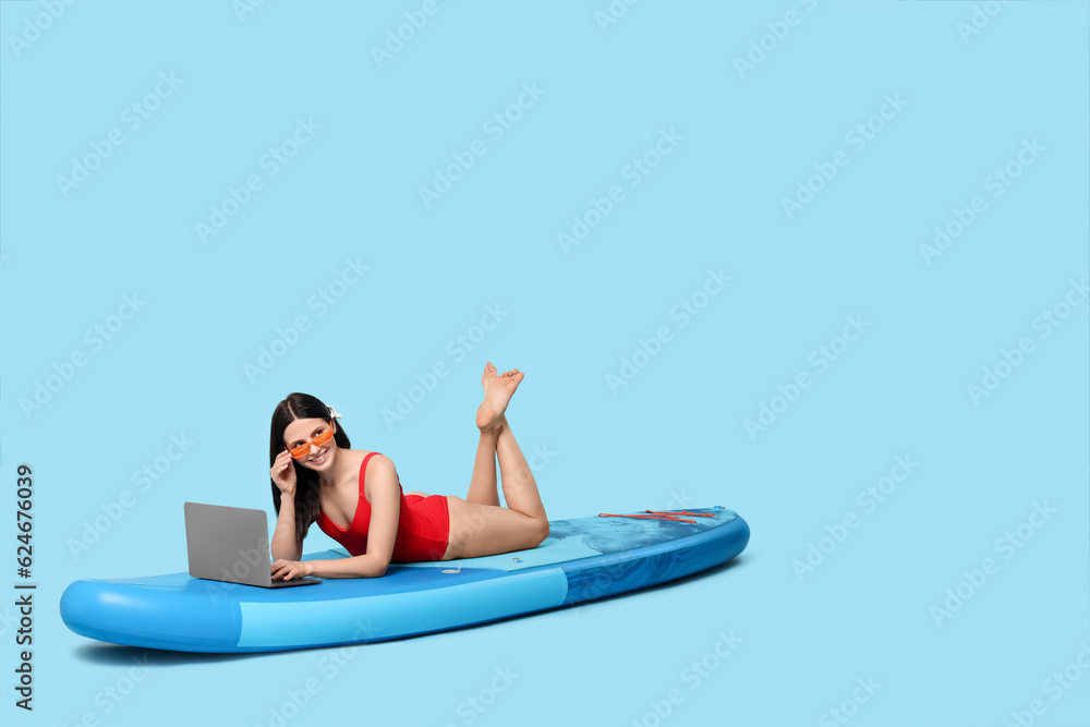 Happy woman with laptop on SUP board against light blue background Happy woman with laptop on SUP board against light blue background