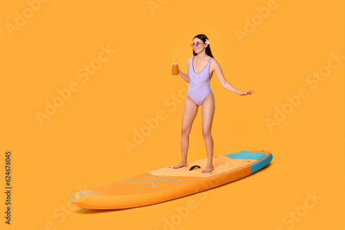 Happy woman with refreshing drink chilling on SUP board against orange background © New Africa