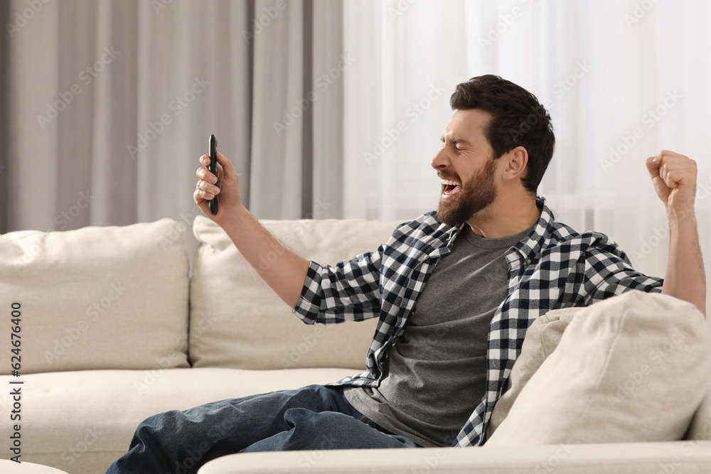 Obraz premium Excited man watching TV on sofa at home