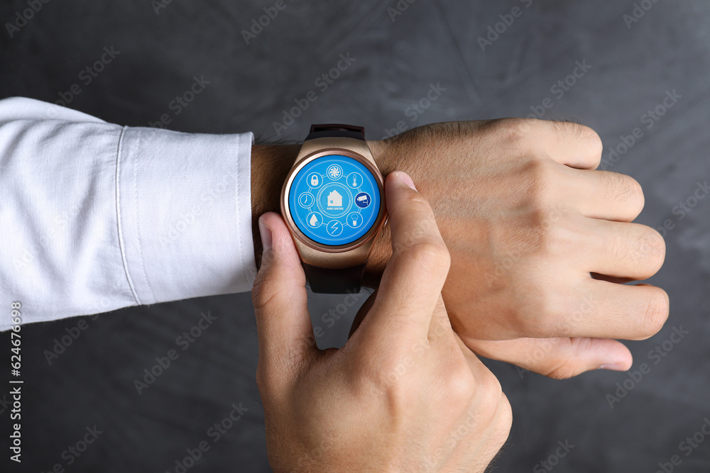 Man setting smart home control system via smartwatch against dark grey background, closeup. App interface with icons on display Man setting smart home control system via smartwatch against dark grey background, closeup. App interface with icons on display