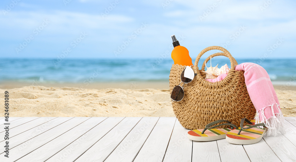 Obraz premium Summer vacation. Bag with sunscreen and accessories on sunny ocean beach, space for text. Banner design
