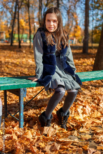 portrait of a girl in an autumn city park, a child sitting on a bench and enjoying the beautiful nature, bright sunlight and maple leaves in a glade