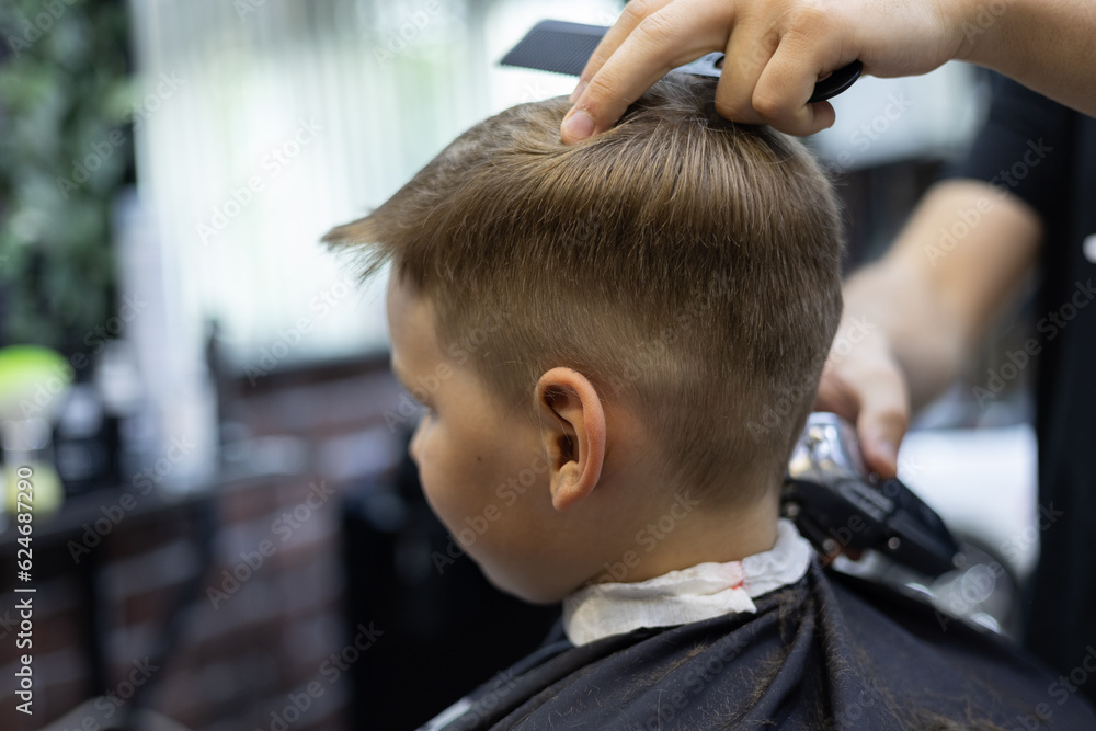 A child in a hairdresser does a hairstyle. The child sits quietly in the chair while the hairdresser works with scissors The hairdresser works in a hairdressing salon to make a hairstyle for a child. A child in a hairdresser does a hairstyle. The child sits quietly in the chair while the hairdresser works with scissors The hairdresser works in a hairdressing salon to make a hairstyle for a child.