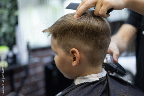 A child in a hairdresser does a hairstyle. The child sits quietly in the chair while the hairdresser works with scissors The hairdresser works in a hairdressing salon to make a hairstyle for a child. © Александр Лебедько