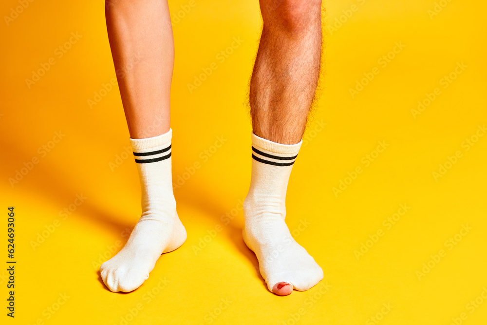 Male and female legs standing in white socks against bright yellow studio background. Hairy and smooth legs. Concept of creativity, imagination and inspiration, fashion, ad. Pop art Male and female legs standing in white socks against bright yellow studio background. Hairy and smooth legs. Concept of creativity, imagination and inspiration, fashion, ad. Pop art