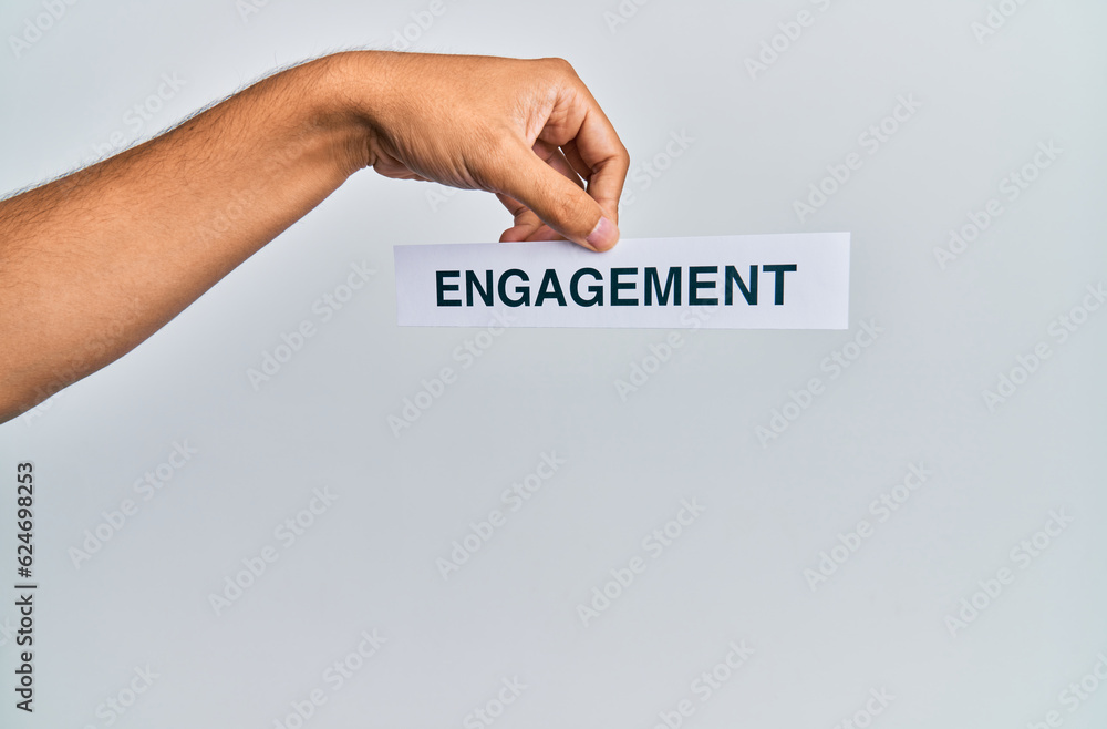 Hand of caucasian man holding paper with engagement word over isolated white background Hand of caucasian man holding paper with engagement word over isolated white background
