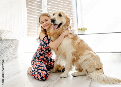 Cute little girl hugging with beautiful goden retriever dog at home