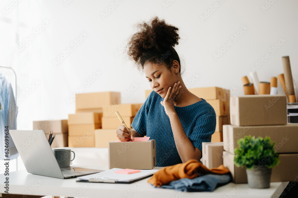 Young African business owner woman prepare parcel box and standing check online orders for deliver to customer on tablet, laptop Shopping Online concept. in office