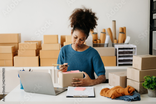 Young African business owner woman prepare parcel box and standing check online orders for deliver to customer on tablet, laptop Shopping Online concept. in office