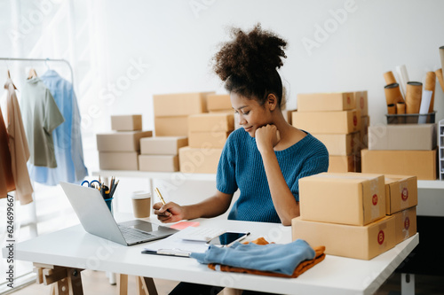 Young African business owner woman prepare parcel box and standing check online orders for deliver to customer on tablet, laptop Shopping Online concept. in office